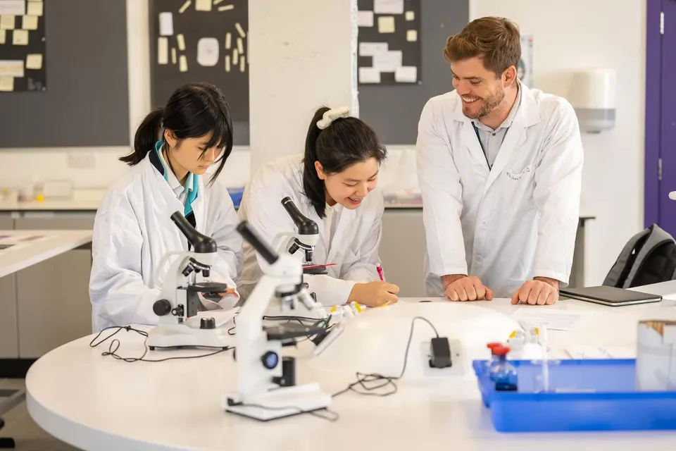 Due studentesse e un insegnante in camice da laboratorio lavorano con microscopi alla Nord Anglia International School Dublin.