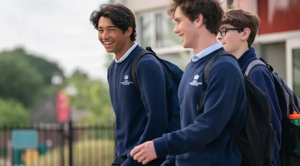 Tre studenti in divisa blu marina sono insieme nell'area esterna della British International School Houston e sorridono.