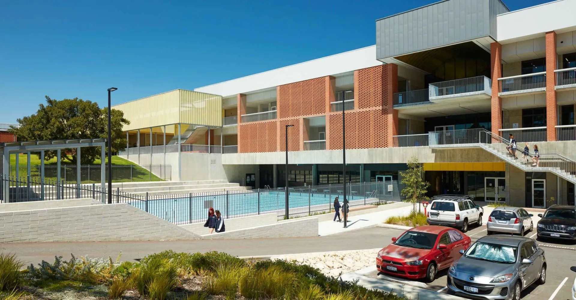 L'edificio a più piani della Balcatta Senior High School, con una piscina in primo piano e auto parcheggiate, è circondato da molto verde.