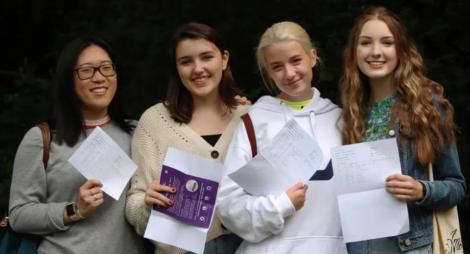 Quattro studentesse della Godolphin School tengono in mano dei fogli sorridendo su uno sfondo scuro.