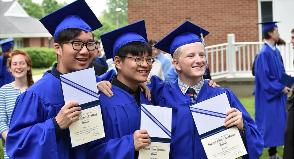 Un gruppo di diplomati della Grand River Academy con tocco e toga blu posa davanti a un edificio in mattoni tenendo in mano i diplomi.