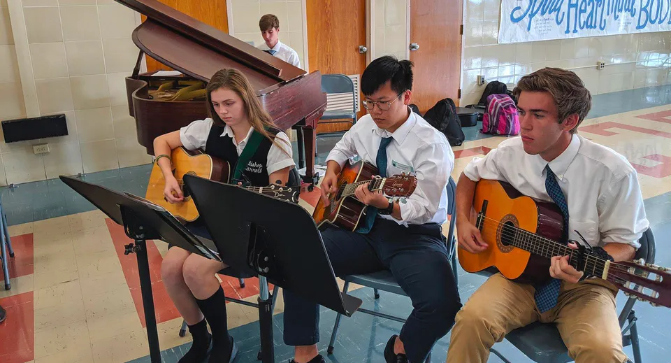 Un gruppo di studenti suona le chitarre e si esibisce con altri strumenti nel campus della Bishop Carroll High School.