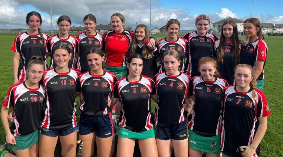 Un gruppo di giovani atlete posa sul campo sportivo del Colaiste Muire (Cobh) sotto un cielo nuvoloso.