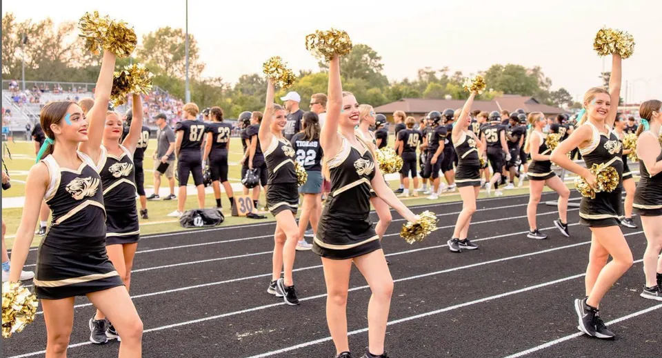 Un gruppo di cheerleader del Blue Valley School District si esibisce su un campo sportivo davanti agli spettatori.