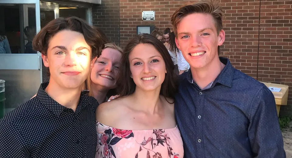 Un gruppo di quattro persone sta in piedi sorridente davanti a un edificio in mattoni nel campus della Eastview Secondary School.