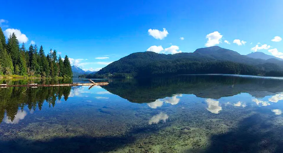 Un lago calmo con boschi e montagne riflette il paesaggio nella zona della Brooks Secondary School.