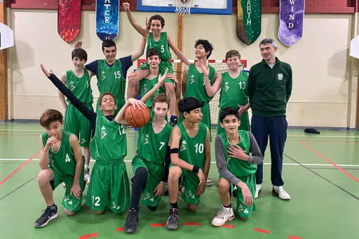 Uno studente della Ermitage International School è in piedi con un pallone da calcio su un campo in erba, con il cielo blu e alberi sullo sfondo.