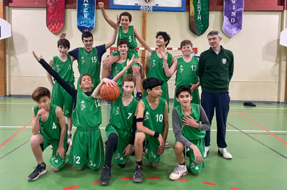 Uno studente della Ermitage International School è in piedi con un pallone da calcio su un campo in erba, con il cielo blu e alberi sullo sfondo.