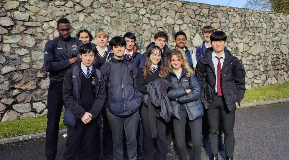 Un gruppo di studenti in uniforme scolastica si trova davanti a un muro di pietra all'interno del campus della Colaiste Muire Mathair.