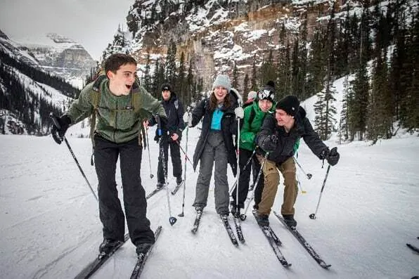 Grupo de jóvenes practicando esquí en un paisaje nival rodeado de montañas y pinos