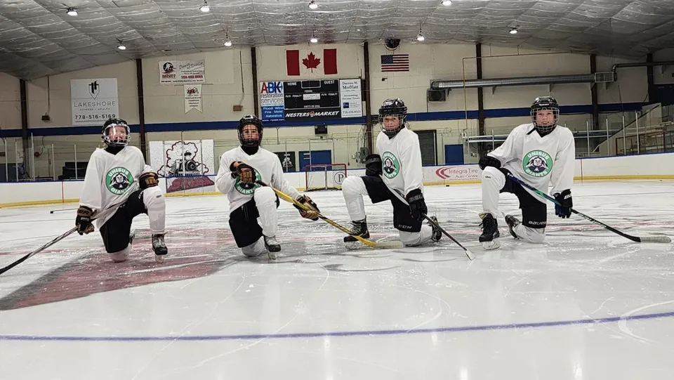 Un gruppo di giocatori di hockey in divisa si trova sulla pista di ghiaccio della Unisus School con la bandiera canadese e americana sullo sfondo.