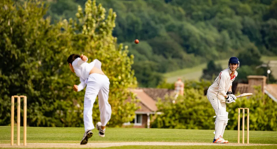 Due giocatori di cricket in divisa bianca giocano una partita sul campo verde della Dauntsey’s School.