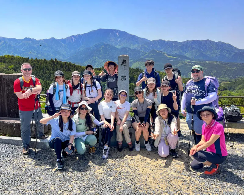 Eine Gruppe von Schülern der Canadian Academy posiert vor einer Berglandschaft unter klarem, blauem Himmel.