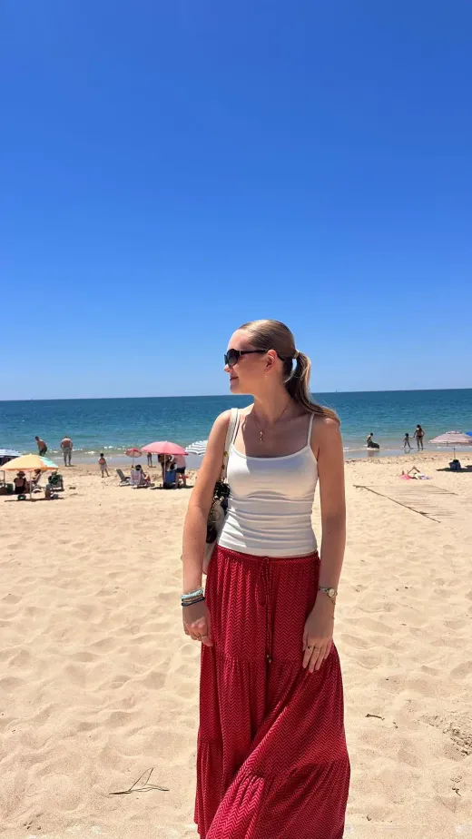 Ragazza con top bianco e gonna rossa su una spiaggia soleggiata spagnola con ombrelloni
