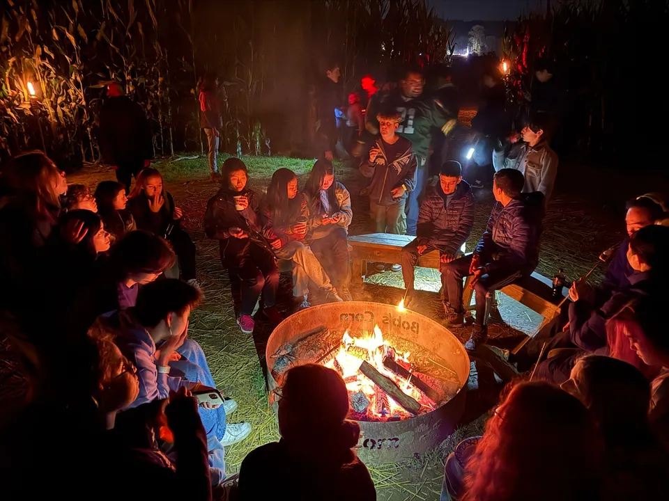 Un gruppo di studenti della Washington Preparatory School è seduto all'aperto attorno a un fuoco da campo, chiacchierando.
