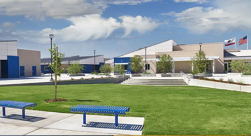 Prato ben curato con panchine blu davanti a edifici moderni nel campus del Clovis Unified School District.
