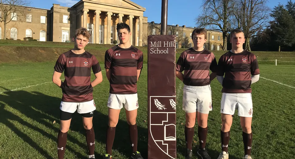 Un gruppo di studenti in divisa sportiva è in piedi davanti all'edificio scolastico della Mill Hill School.