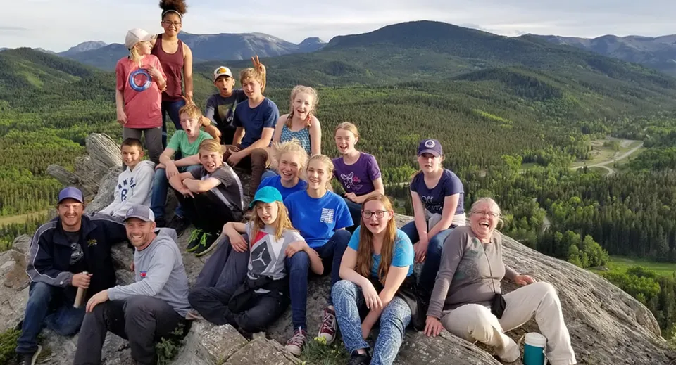Un gruppo di studenti, studentesse e adulti della Prairie Christian Academy si trova su una roccia e guarda verso montagne boscose.