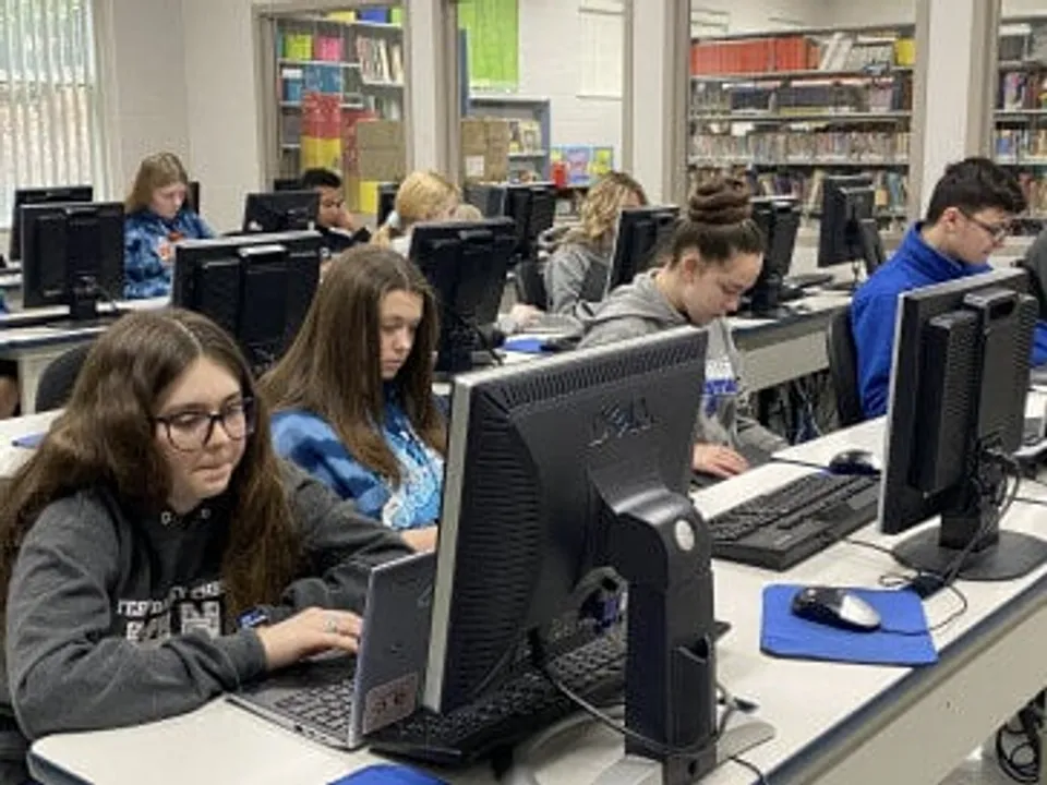 Studenti della Teays Valley Christian School lavorano al computer in un'aula con libri e materiale didattico sullo sfondo.