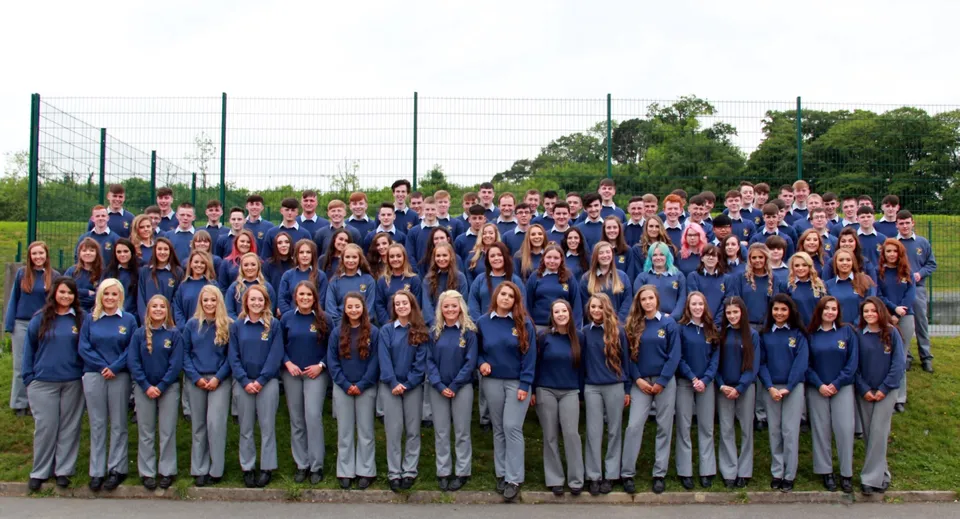 Un grande gruppo di studenti del Breifne College sta insieme all'aperto con uno sfondo di alberi e tralicci elettrici.
