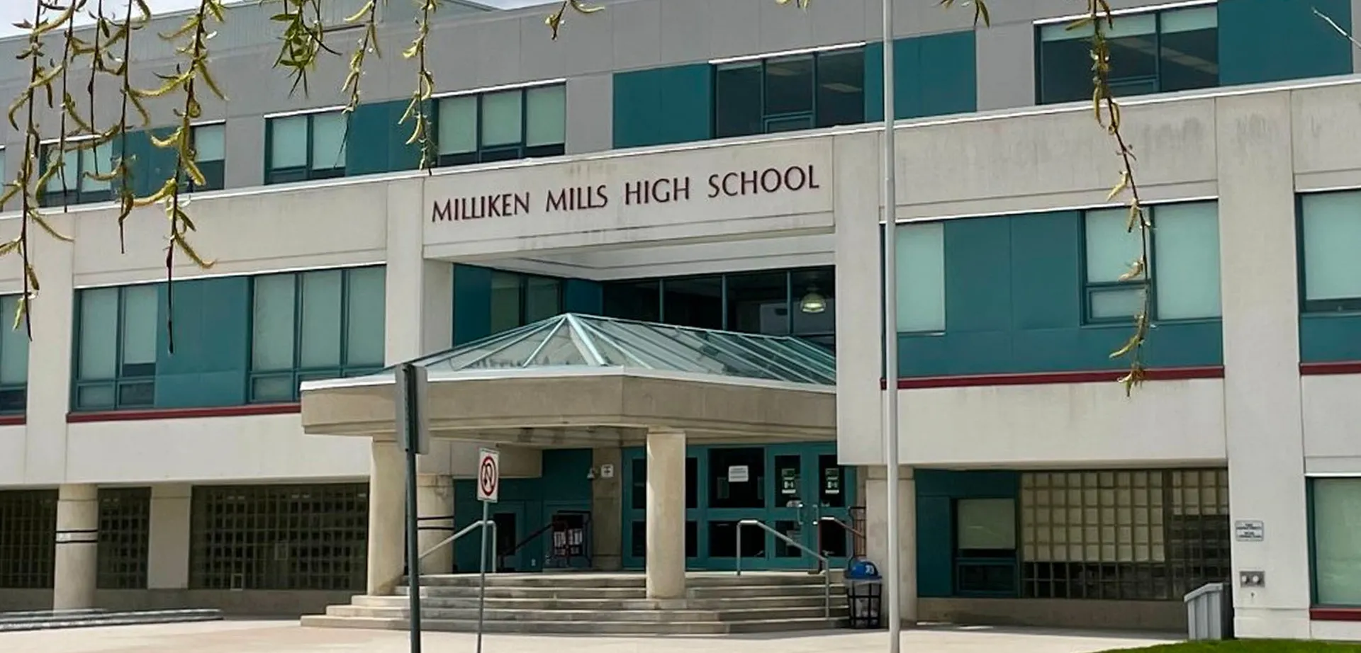 L'ingresso del moderno edificio della Milliken Mills Secondary School è realizzato in vetro e cemento ed è circondato da piante pendenti.