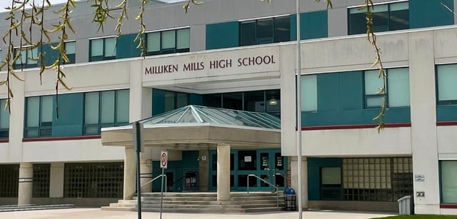 L'ingresso del moderno edificio della Milliken Mills Secondary School è realizzato in vetro e cemento ed è circondato da piante pendenti.