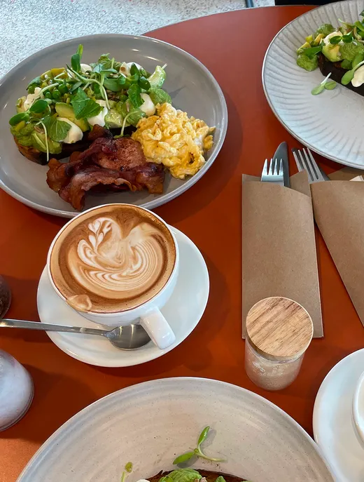 Desayuno con tostada de aguacate, beicon, huevos revueltos y capuchino