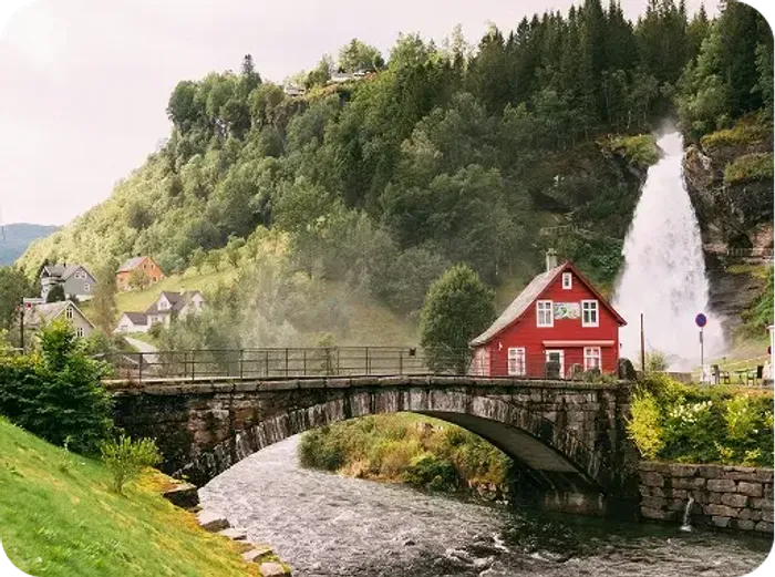 Casa rossa e cascata su una collina verde in Norvegia, con un ponte di pietra sopra il torrente