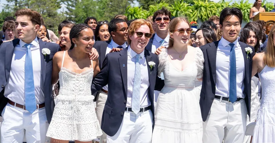 Un gruppo di studenti della Hotchkiss School si raccoglie all'aperto davanti a palme e a un paesaggio verde.