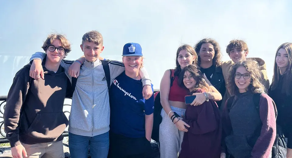 Un gruppo di studenti e studentesse si trova all'aperto nel terreno della Bayside Secondary School sotto un cielo limpido.