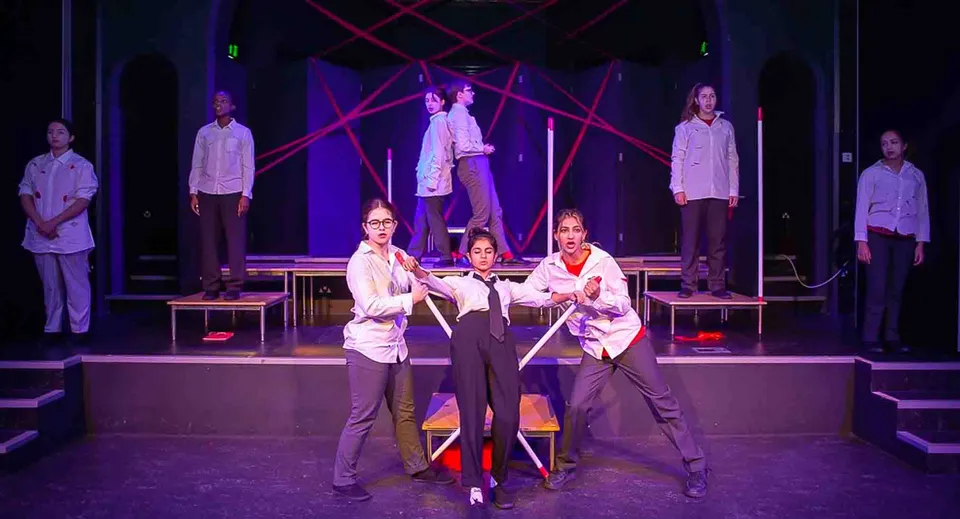 Gli studenti della St. Margaret’s School mettono in scena sul palco una produzione teatrale o musicale con luci colorate e motivi geometrici sullo sfondo.