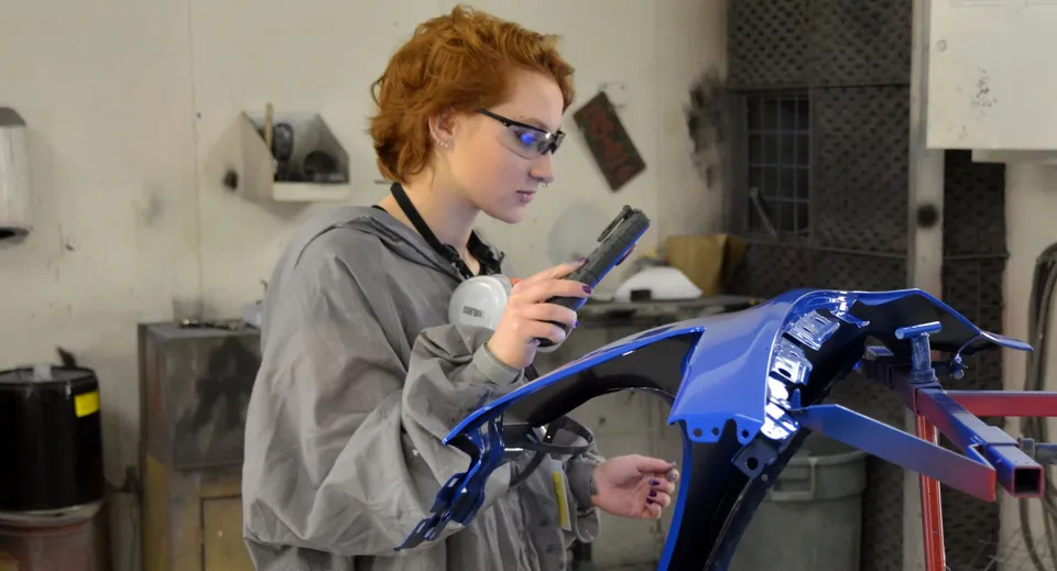 Una persona lavora a una moto blu nell'officina della Napanee District Secondary School.