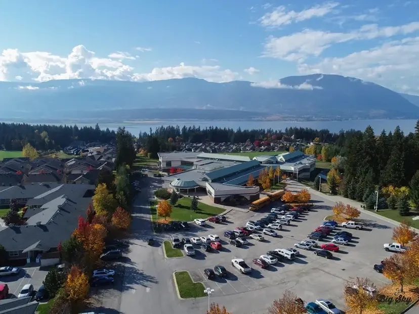 Vista aerea del campus della Salmon Arm Secondary con parcheggio, alberi e montagne con un lago sullo sfondo.