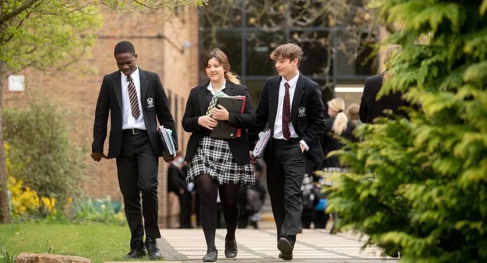 Tre persone camminano insieme su un viale alberato nel campus della Bloxham School.