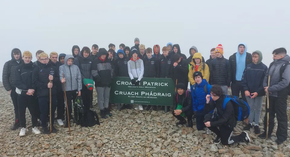 Un gruppo di studentesse e studenti del St. Coleman's College si trova davanti al cartello Croagh Patrick in un paesaggio montano roccioso.