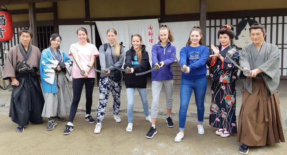 Un gruppo di studenti e studentesse della Lincoln High School indossa abiti tradizionali giapponesi e abbigliamento casual moderno in una stanza giapponese con porte scorrevoli.