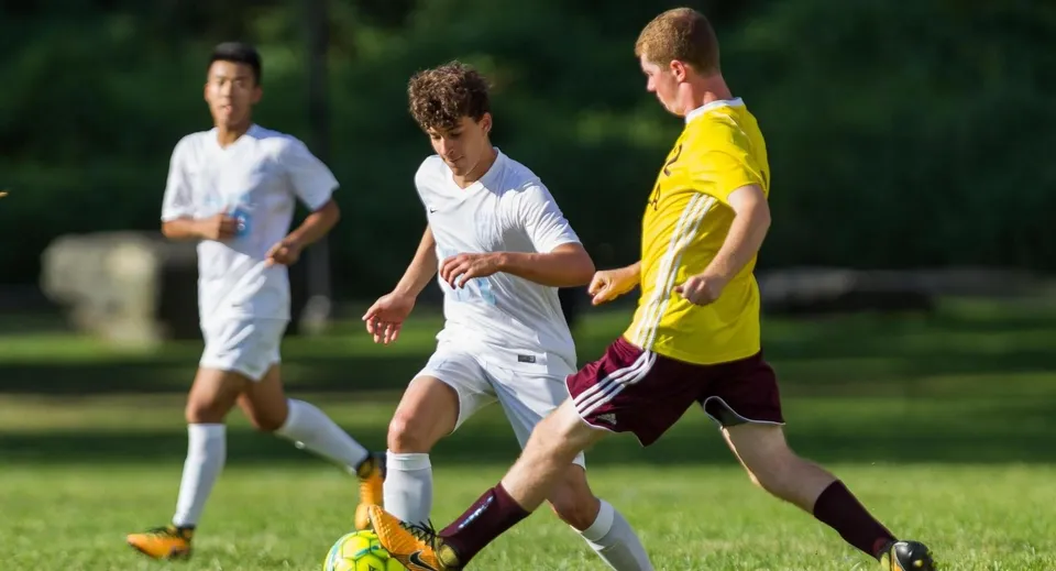 Tre studenti della Léman Manhattan Preparatory School giocano a calcio su un campo erboso.