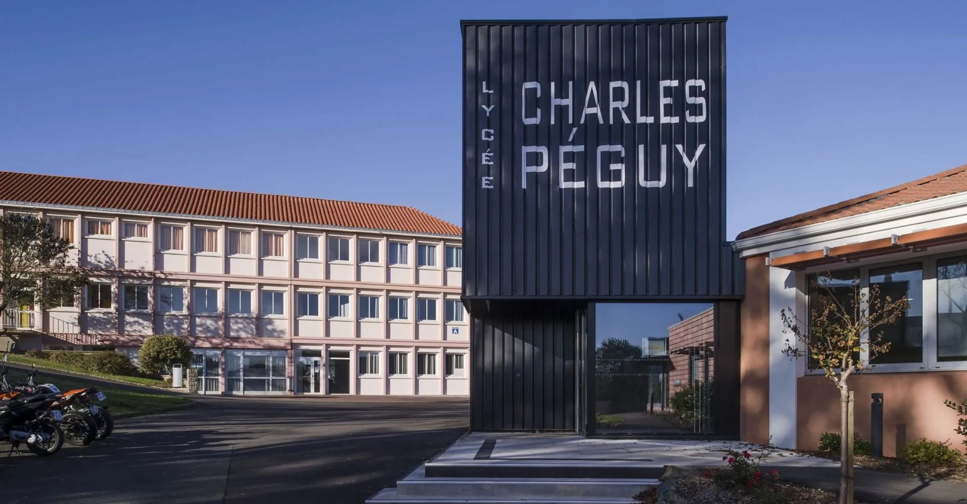 Grande struttura nera con la scritta Charles Péguy davanti a edifici moderni nel campus del Lycée Charles Péguy.