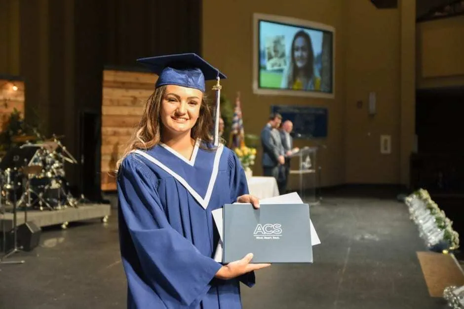 Una joven con traje de graduación sostiene su diploma en el campus de la Abbotsford Christian School.