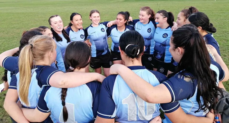 Un gruppo di atlete della Dannevirke High School in divisa blu e bianca si confronta sul campo da gioco.