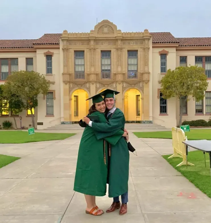 Due diplomati in toga verde si abbracciano davanti alla loro high school