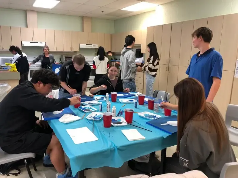 Alumnos pintando cuadros con acuarela azul alrededor de una mesa en clase de arte