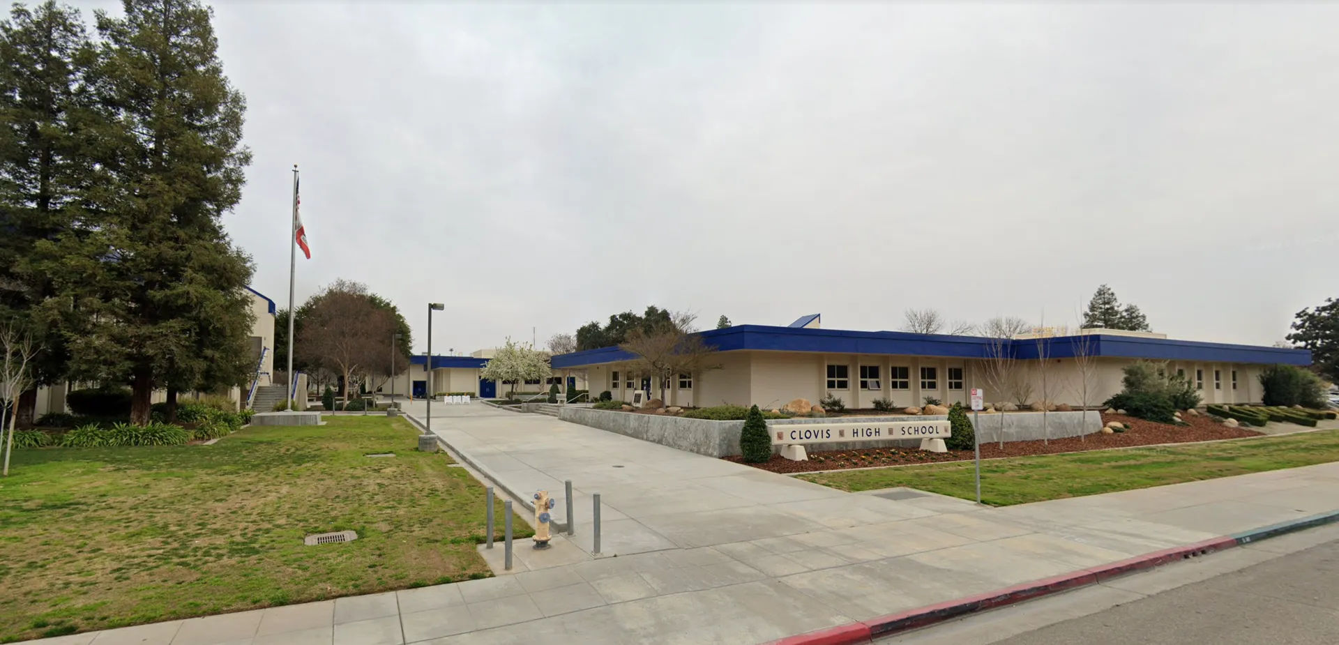 L'edificio della Clovis High School con finiture blu sul tetto, un'insegna con il nome della scuola e un pennone con la bandiera.