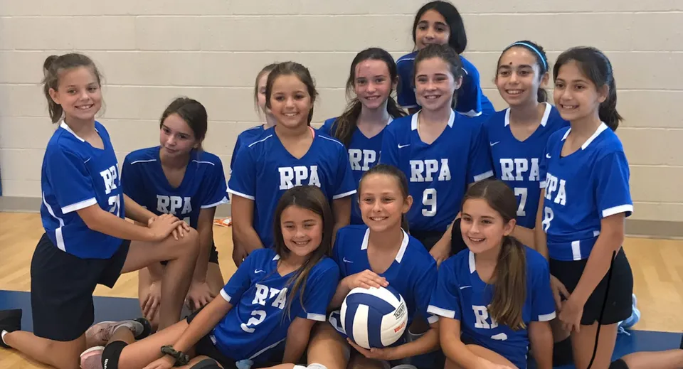 Un gruppo di giovani atlete in divisa blu posa insieme sul campo sportivo della Royal Palm Academy.
