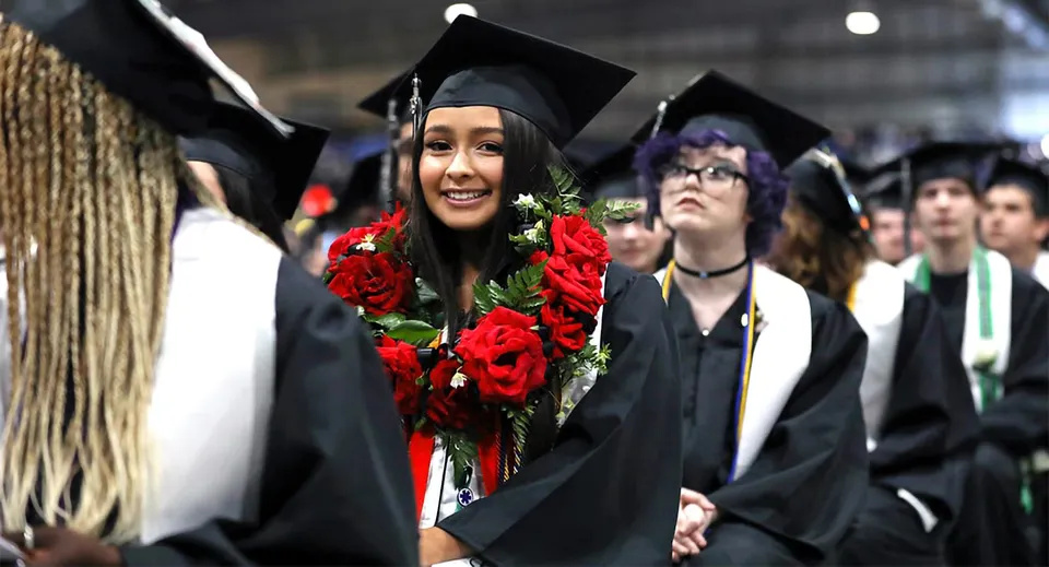 Una giovane donna in toga tiene un mazzo di rose durante la cerimonia di diploma del Green Bay Area Public School District.