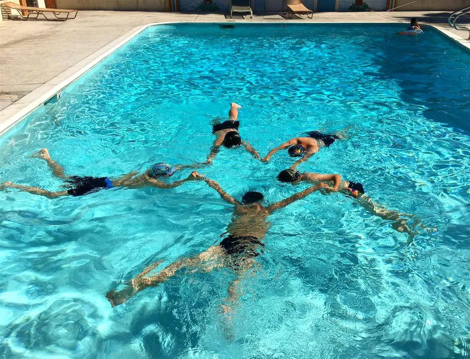 Studenti della South Hills Academy nuotano in piscina tenendosi per mano nell'acqua.