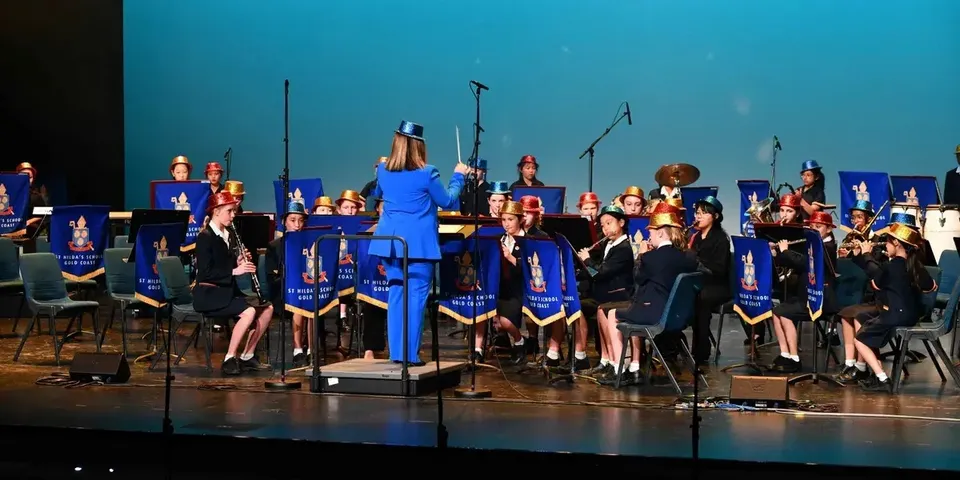 L'orchestra scolastica della St. Hilda’s School suona su un palco sotto la direzione di una direttrice.