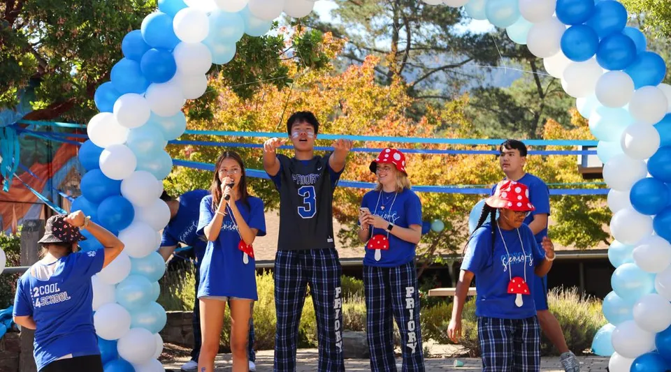 Un gruppo di studentesse e studenti della Woodside Priory School è in piedi davanti a un arco di palloncini all'aperto, con alberi sullo sfondo.