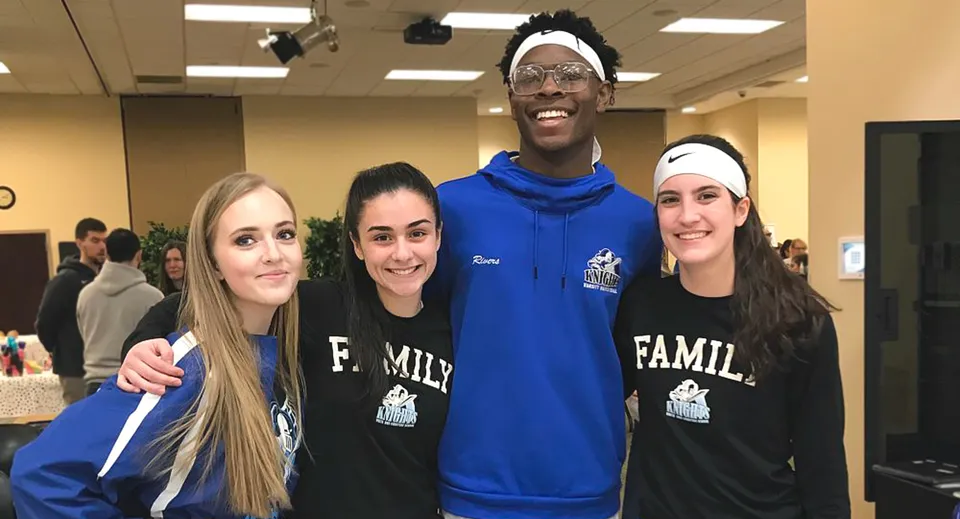 Un gruppo di quattro persone si trova insieme in una stanza della Smithtown Christian School e sorride.