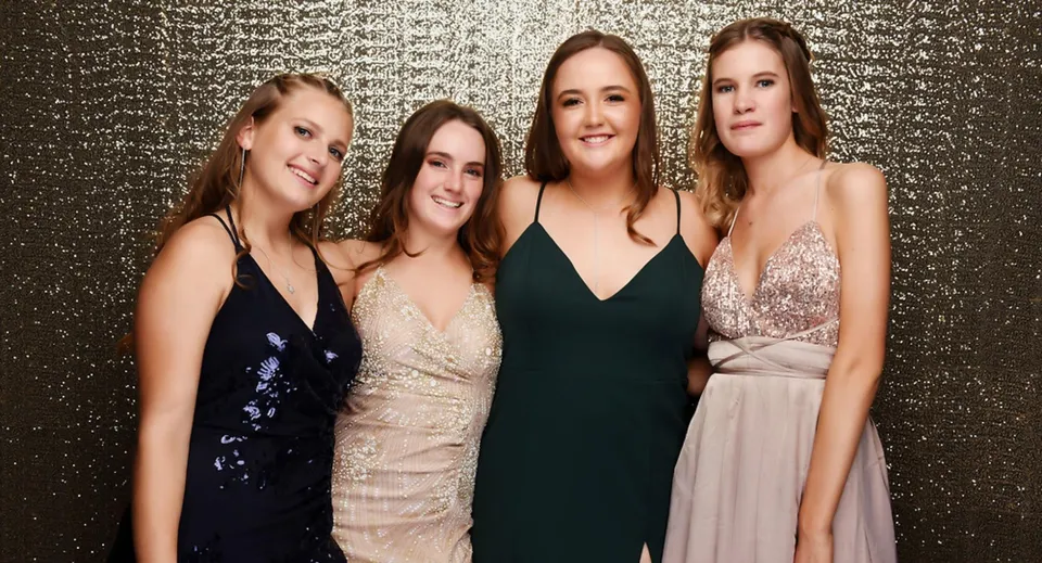 Quattro studentesse in abiti eleganti posano davanti a uno sfondo dorato nel campus del Marist College.